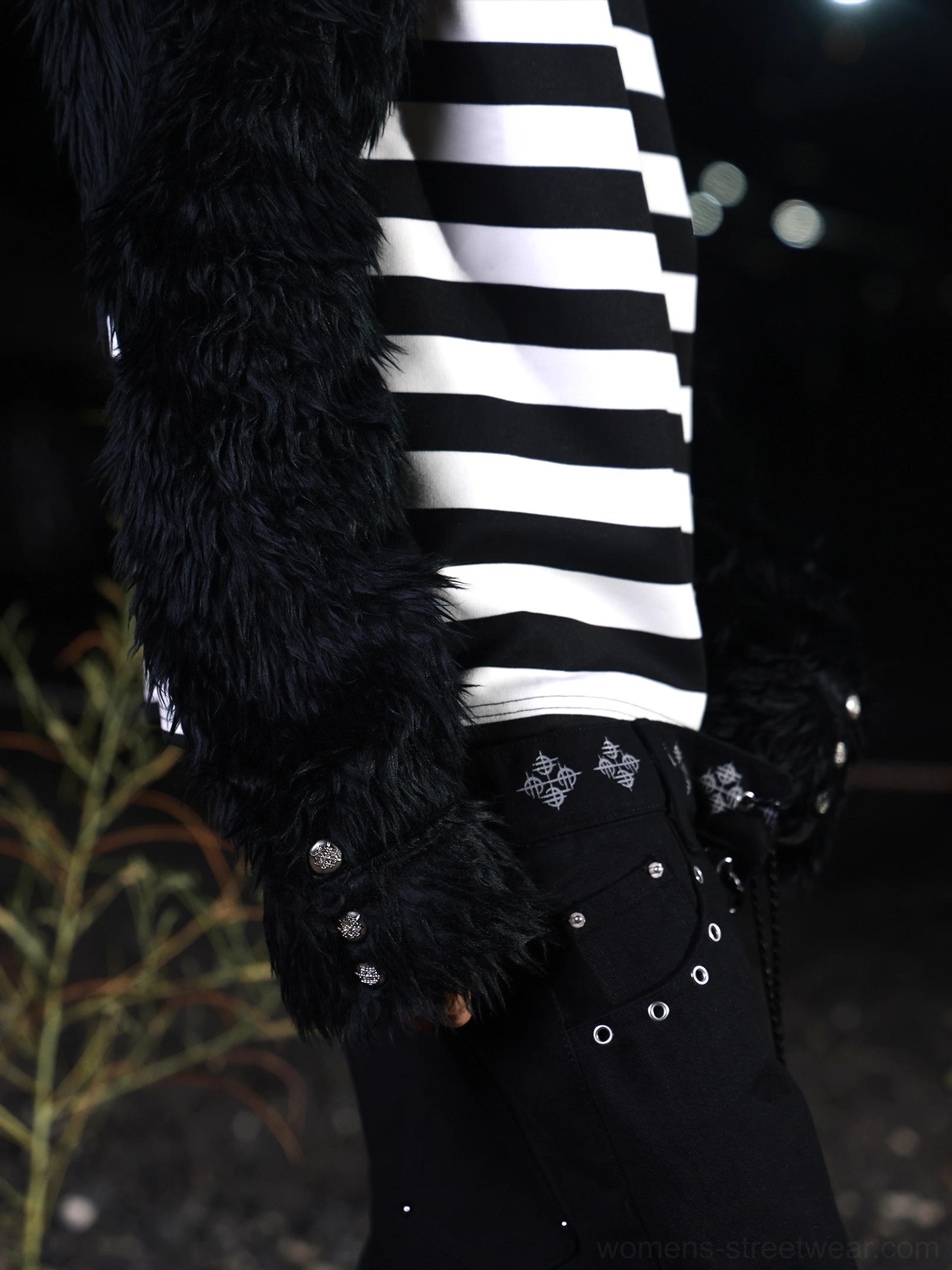 Close-up detail of black faux fur sleeve, black and white horizontal stripes, and decorative metal cuff buttons on a gothic streetwear shirt