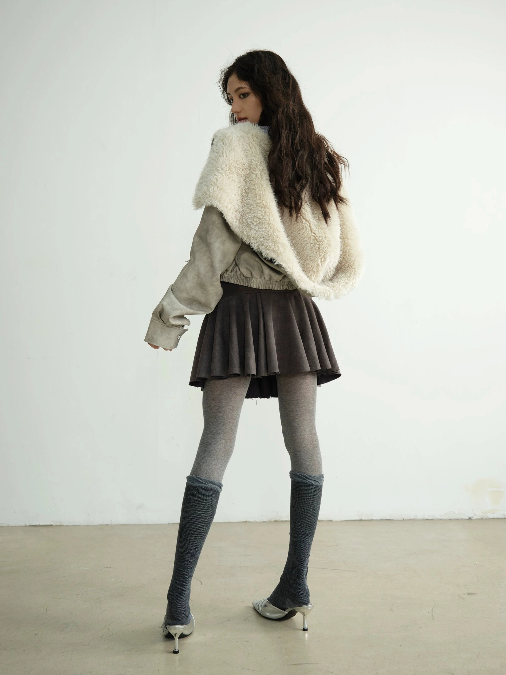 Back three-quarter view of a relaxed faux shearling hooded cropped jacket with oversized fur collar and loose sleeve cuffs