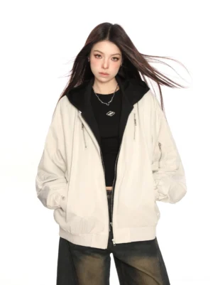 Beige faux two-piece hooded bomber jacket shown from the front with an attached black hood, oversized streetwear fit, zip front, and wide-leg jeans styling