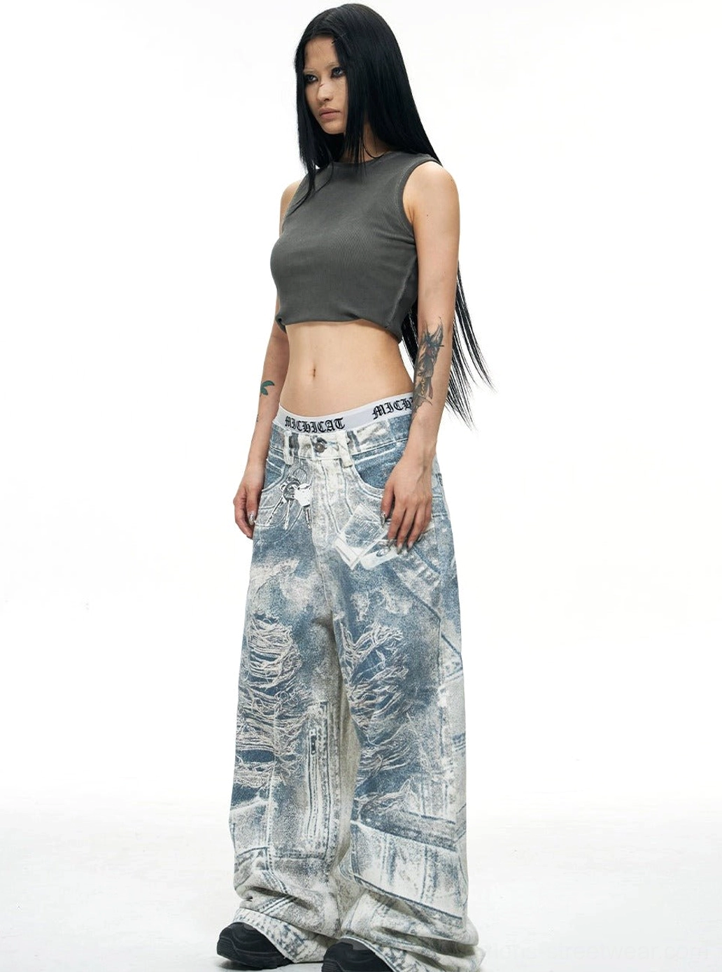 Female model wearing blue acid-wash wide-leg baggy jeans with a cropped gray tank top in a relaxed Y2K streetwear outfit