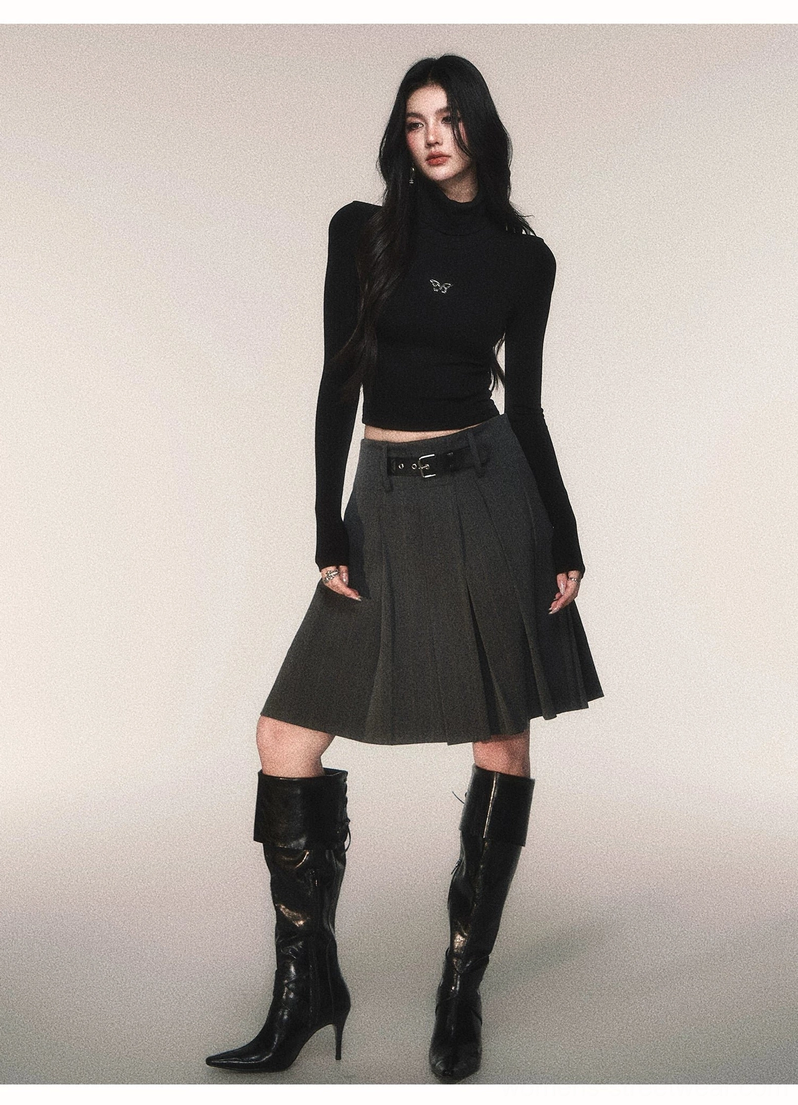 Fitted black butterfly turtleneck crop top paired with grey pleated skirt and tall heeled leather boots