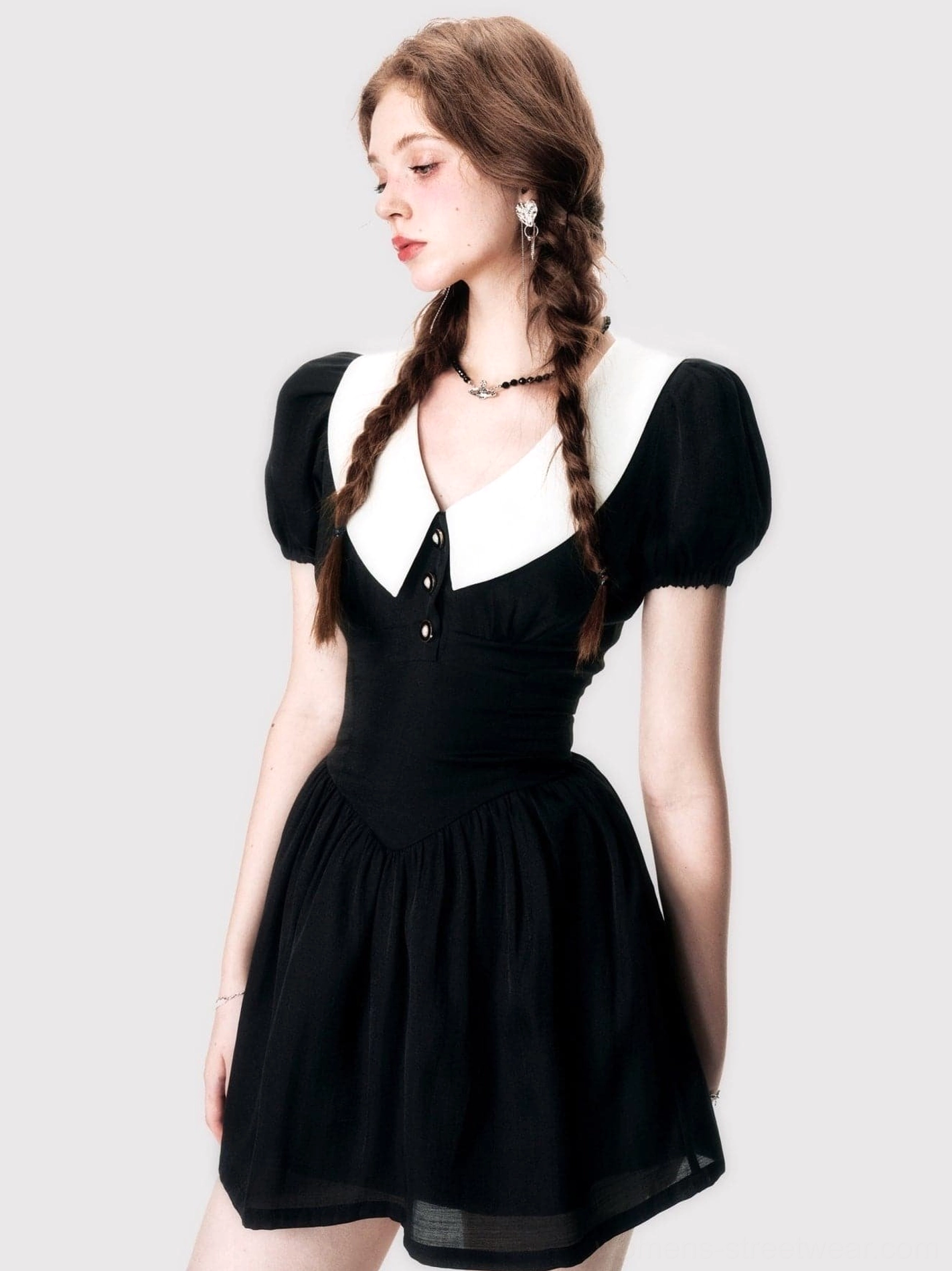 Left side view of a fitted black puff sleeve retro mini dress with white collar, front buttons, high waist, and flared skirt