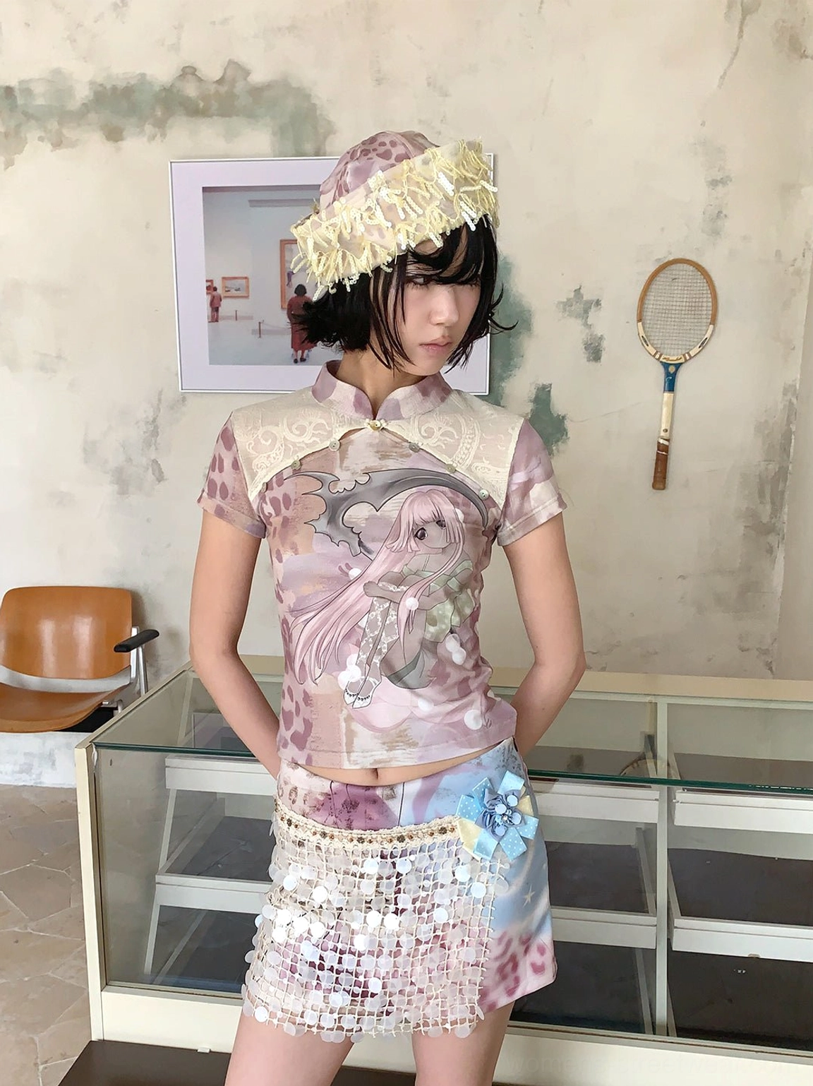 Female model styling a fitted cheongsam collar anime print tee with a straw bucket hat and beaded tie-dye mini skirt