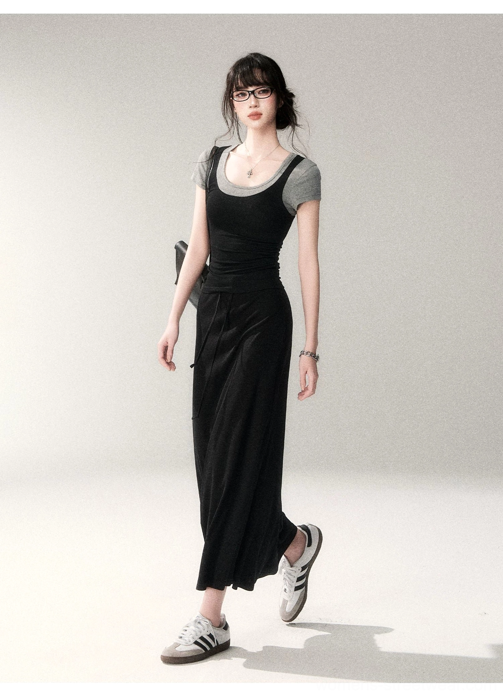 Walking view of a fitted layered scoop neck streetwear top under a black maxi tank dress with retro casual sneakers and minimalist accessories