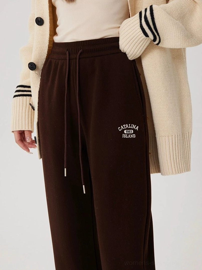 Brown fleece-lined straight-leg streetwear sweatpants styled with a beige knit cardigan and cream top, showing the high-rise drawstring waist and embroidered thigh detail