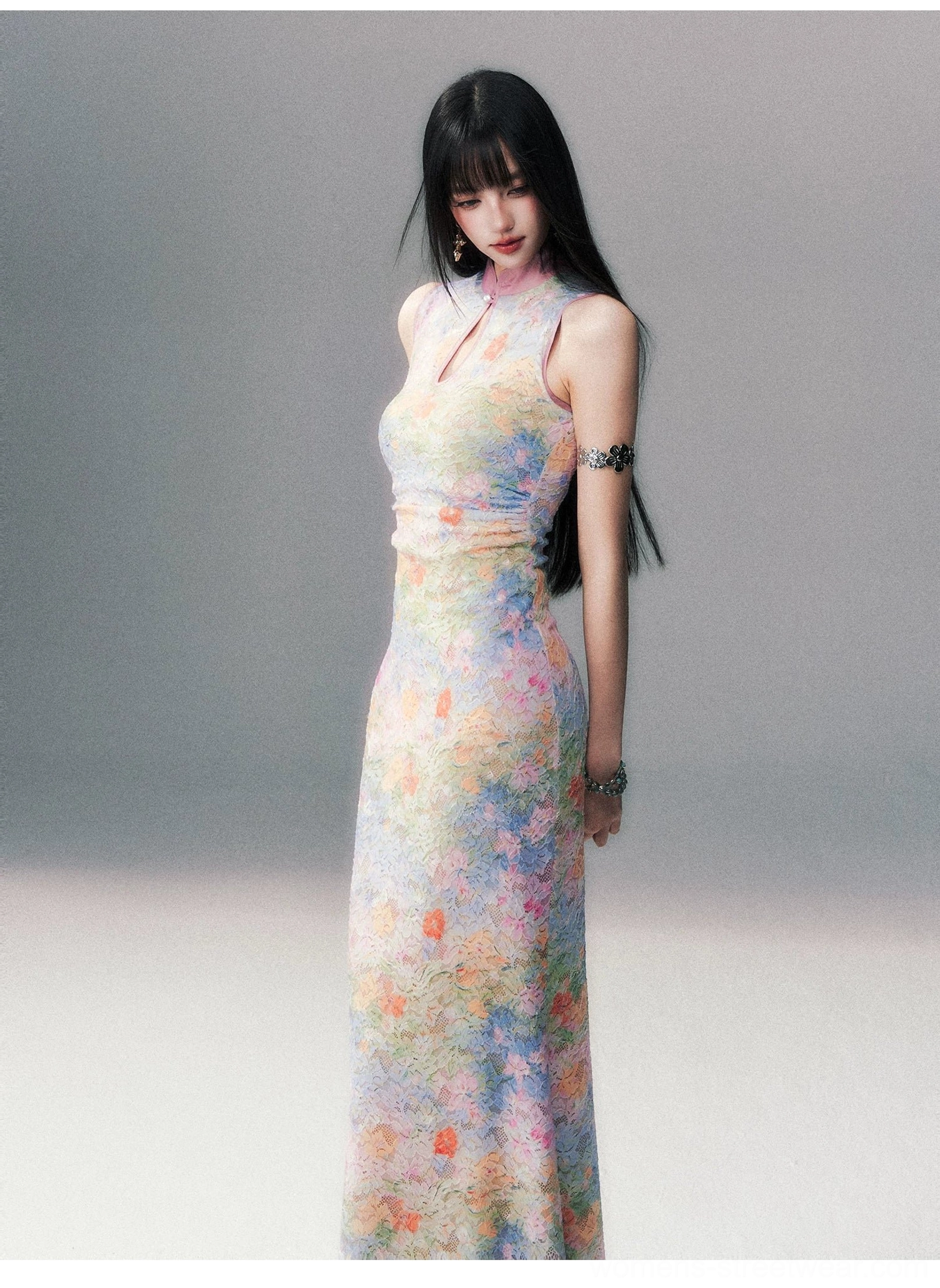 Side view of a woman wearing a floor length fitted watercolor floral cheongsam dress with a halter inspired Mandarin neckline, pastel botanical print, and arm chain accessories