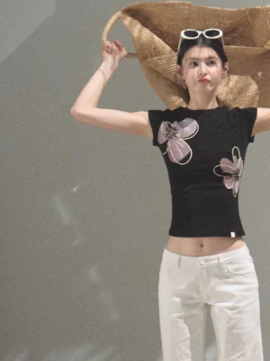 Black floral graphic fitted cropped tee styled with white low-rise pants in a minimalist studio