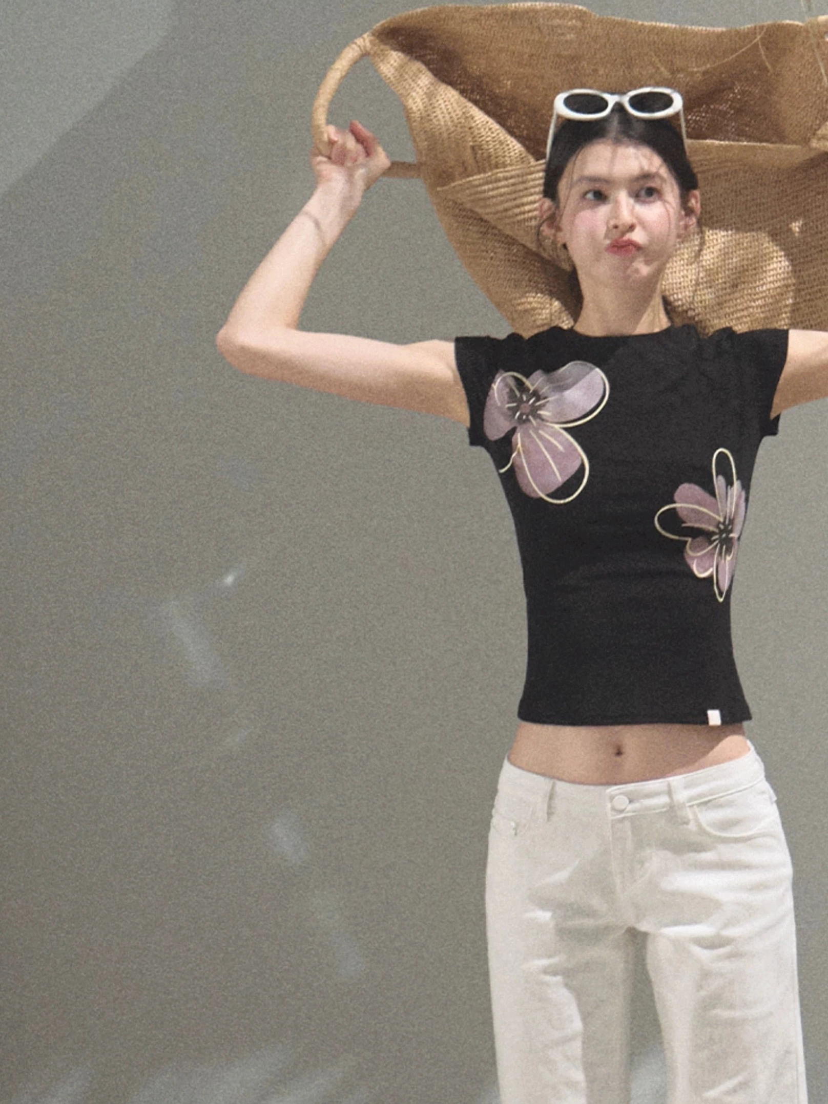 Black floral graphic fitted cropped tee styled with white low-rise pants in a minimalist studio