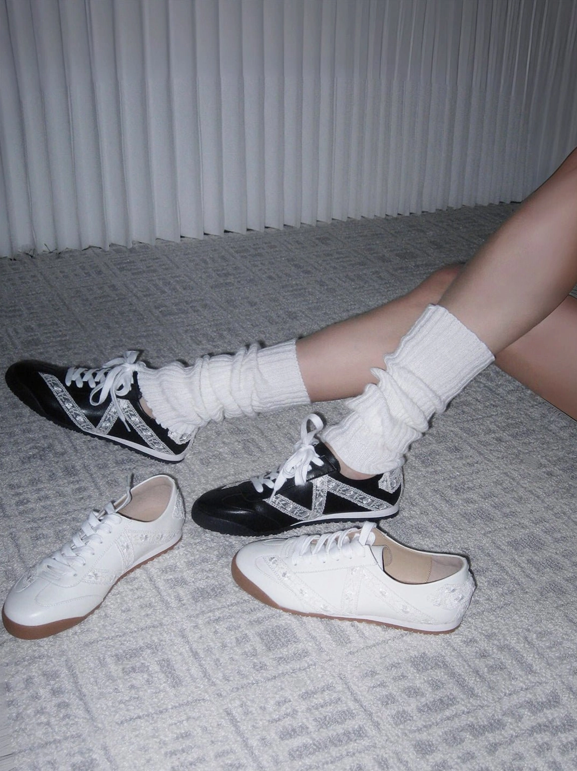 Black and white and all-white floral lace low-profile sneakers styled with ruffled socks on an indoor floor