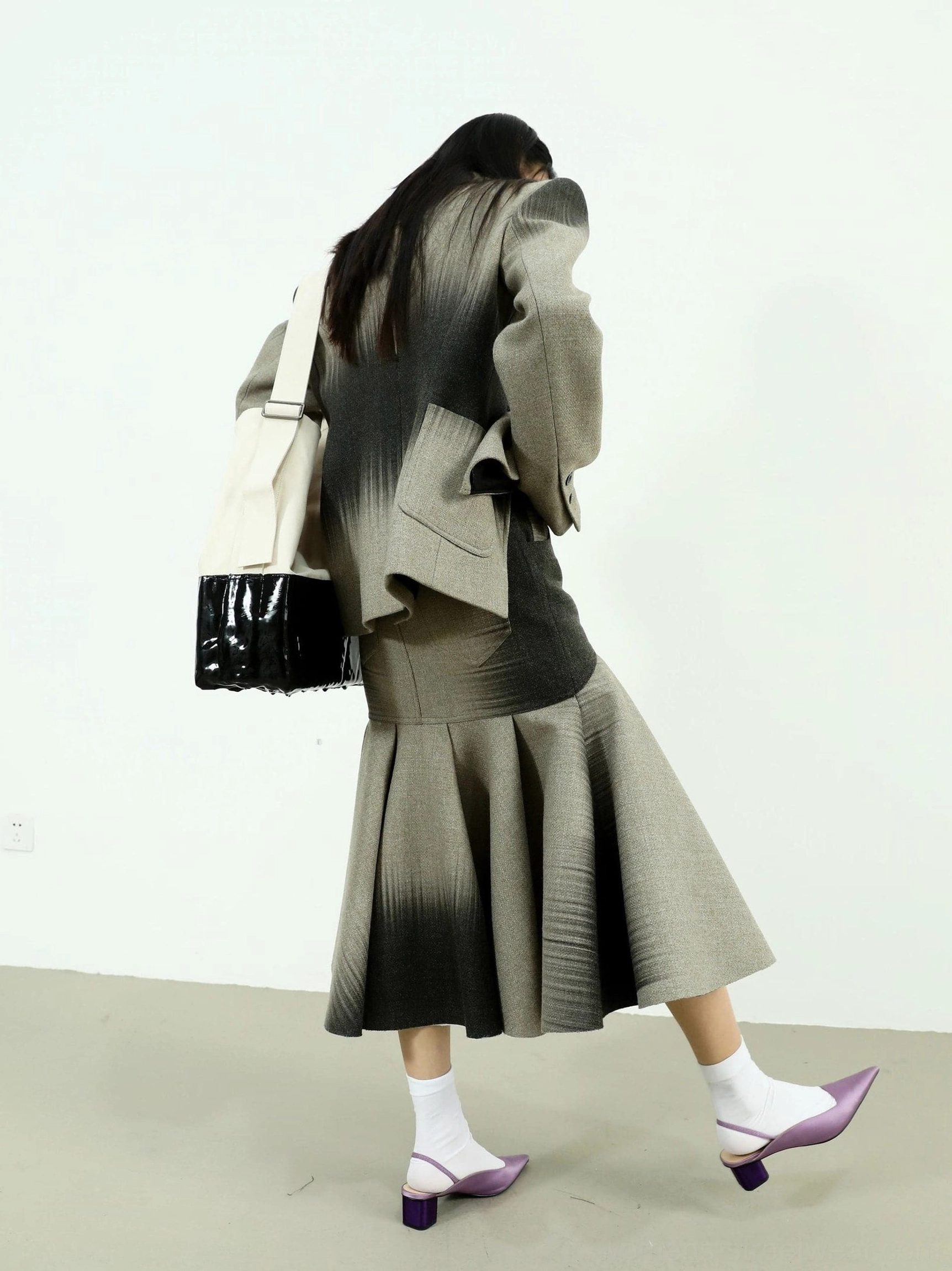 Walking model wearing a flowing gray to black ombre fishtail maxi skirt with purple mule heels and a two-tone tote bag