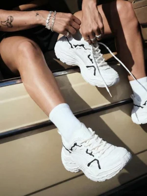 Flux Form white and black chunky leather sneakers worn with white crew socks by tattooed streetwear model beside vintage car
