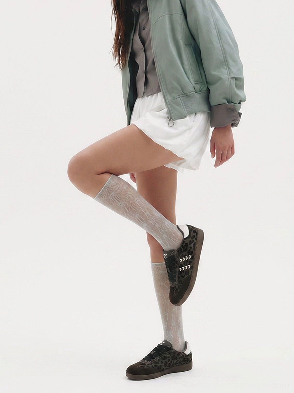 Model wearing forest leopard print low top sneakers with a white mini skirt and sheer socks, showing the full sneaker silhouette and gum outsole