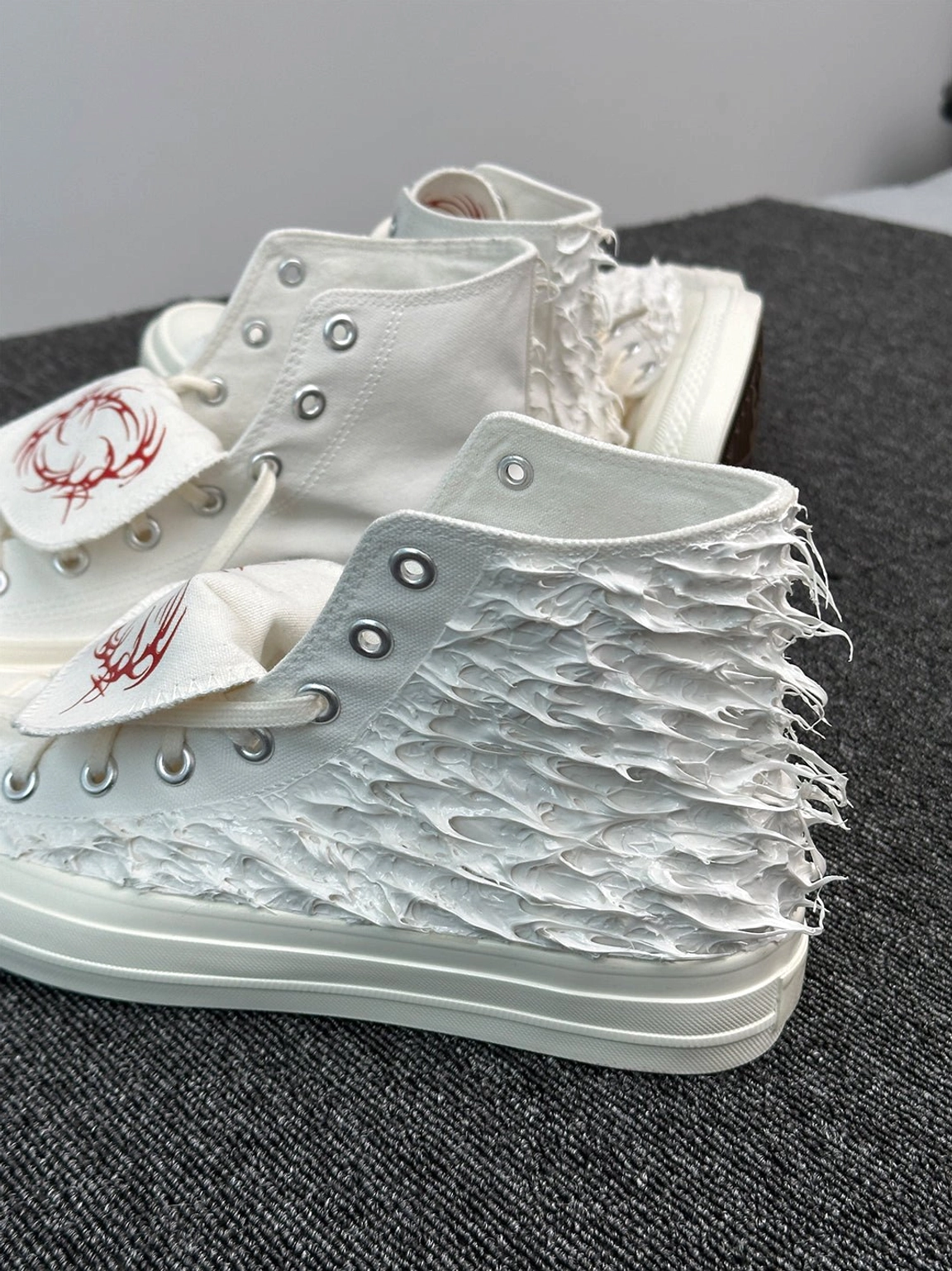 White fringed high-top canvas sneakers with metal eyelets, loose laces and red tribal-inspired tongue detail