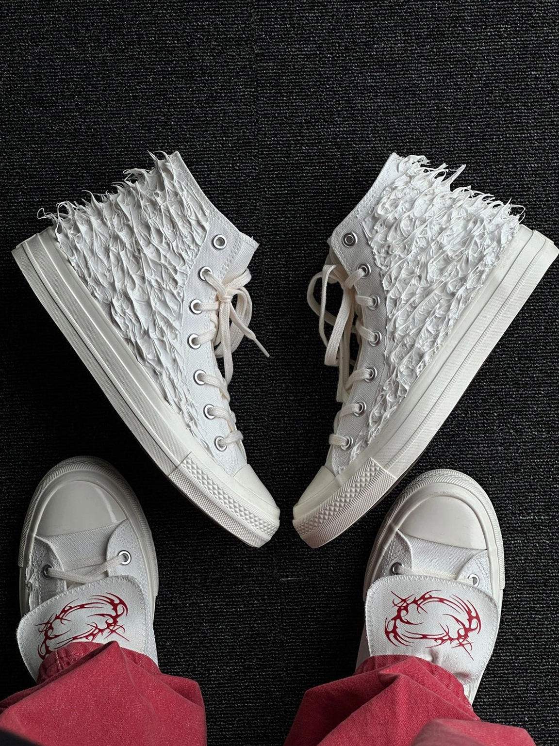 Top view of white fringed high-top canvas sneakers with red tribal-inspired insole print and textured upper