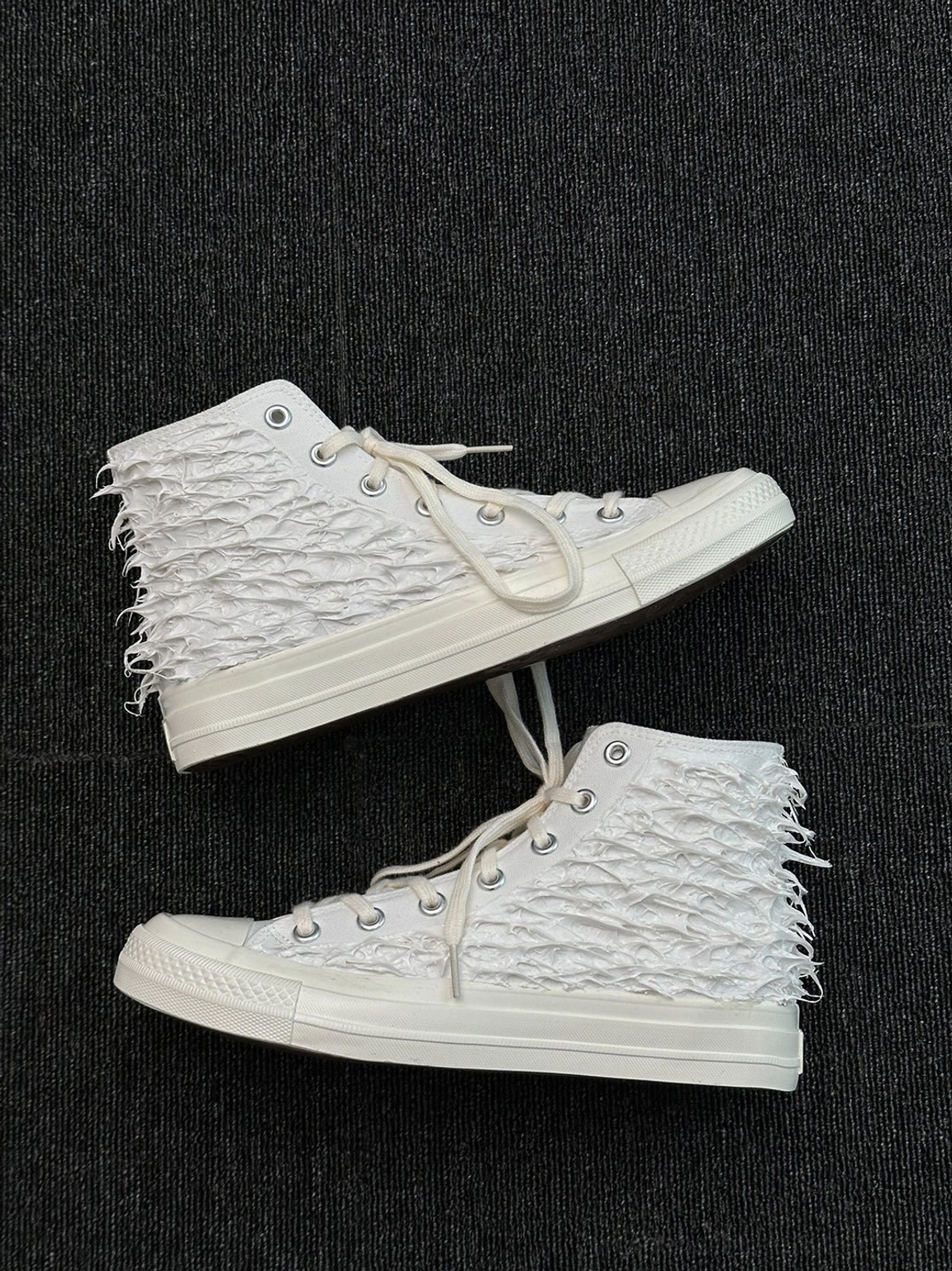 White fringed high-top canvas sneakers arranged in a crossed flat lay showing textured tassel canvas uppers