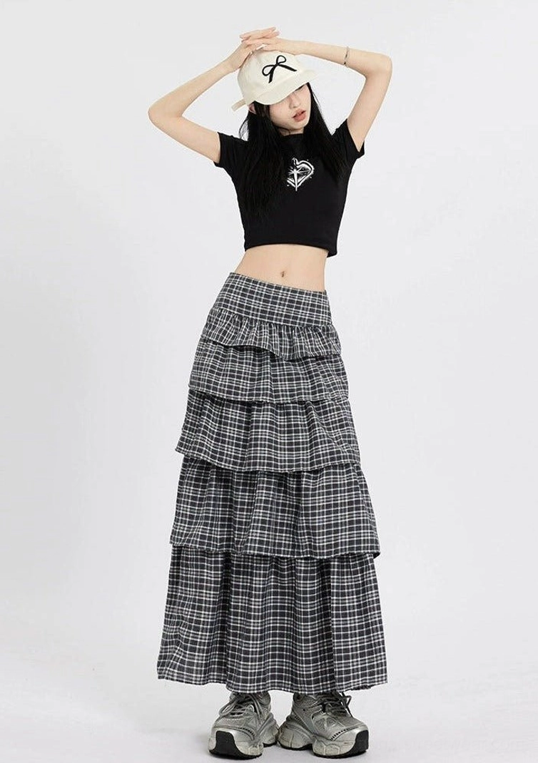 Front view of a dark plaid multi layered ruffle maxi skirt with high waist styled with a black crop top and white cap
