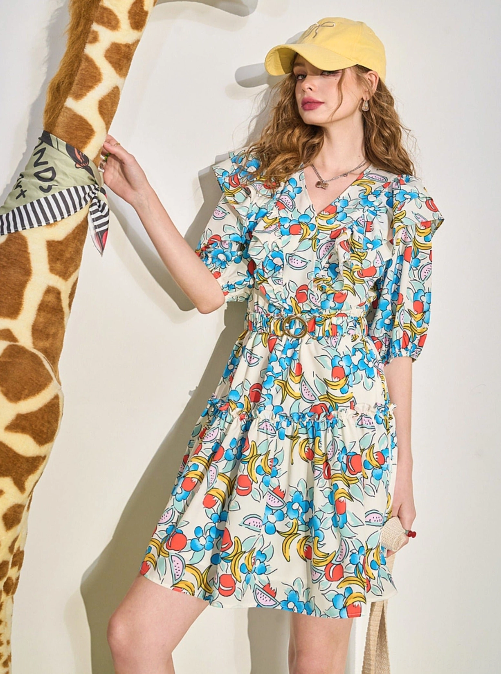 Side view of colorful fruit print ruffle V-neck mini dress styled with a baseball cap and canvas tote bag