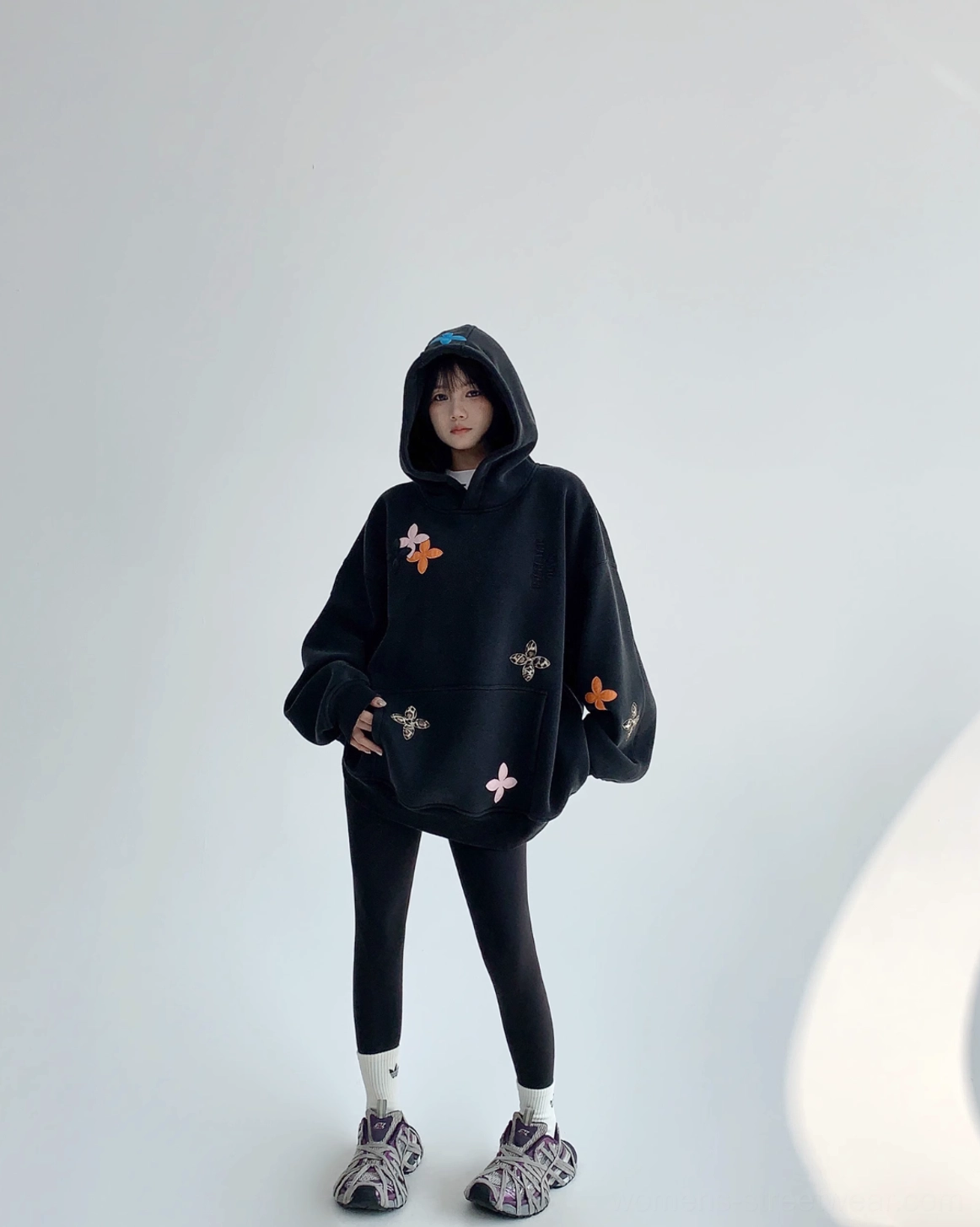 Full-body view of an oversized black embroidered-style floral hoodie paired with leggings and chunky sneakers for a modern streetwear outfit