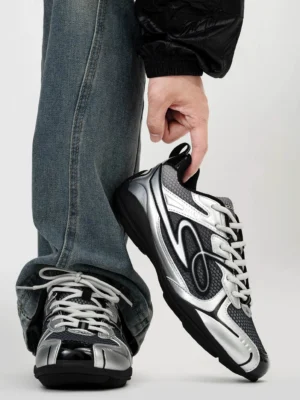 Dark silver futuristic retro runner sneakers held above loose blue denim with metallic overlays black breathable mesh curved wave side detail and lace-up closure