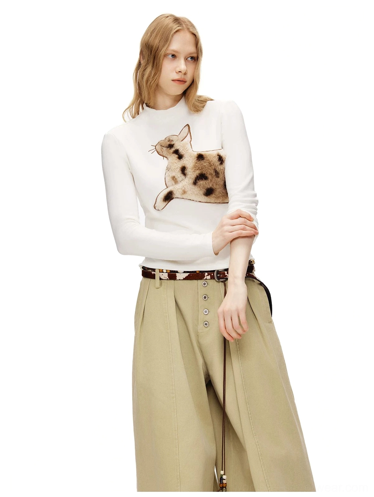 Three-quarter view of a white fuzzy cat graphic mock neck tee paired with khaki wide-leg pants and a leather belt