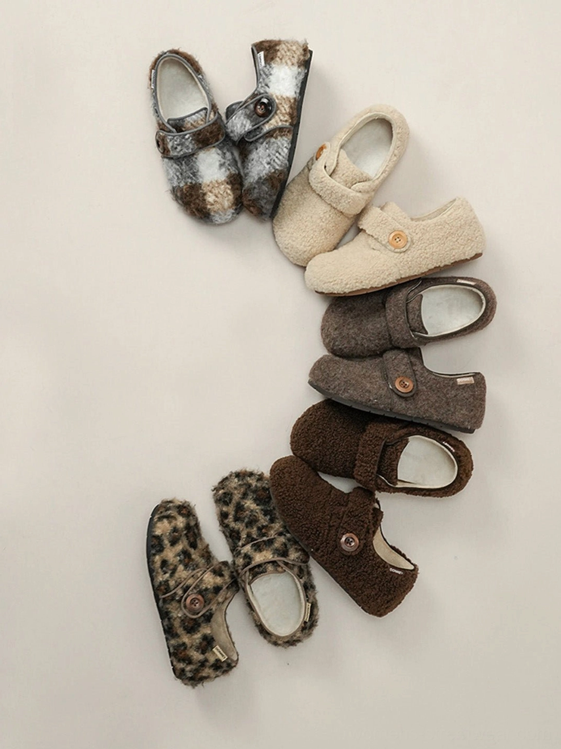 Overhead arrangement of fuzzy faux fur slip-on shoes with signature button-style Velcro straps and rounded toe design