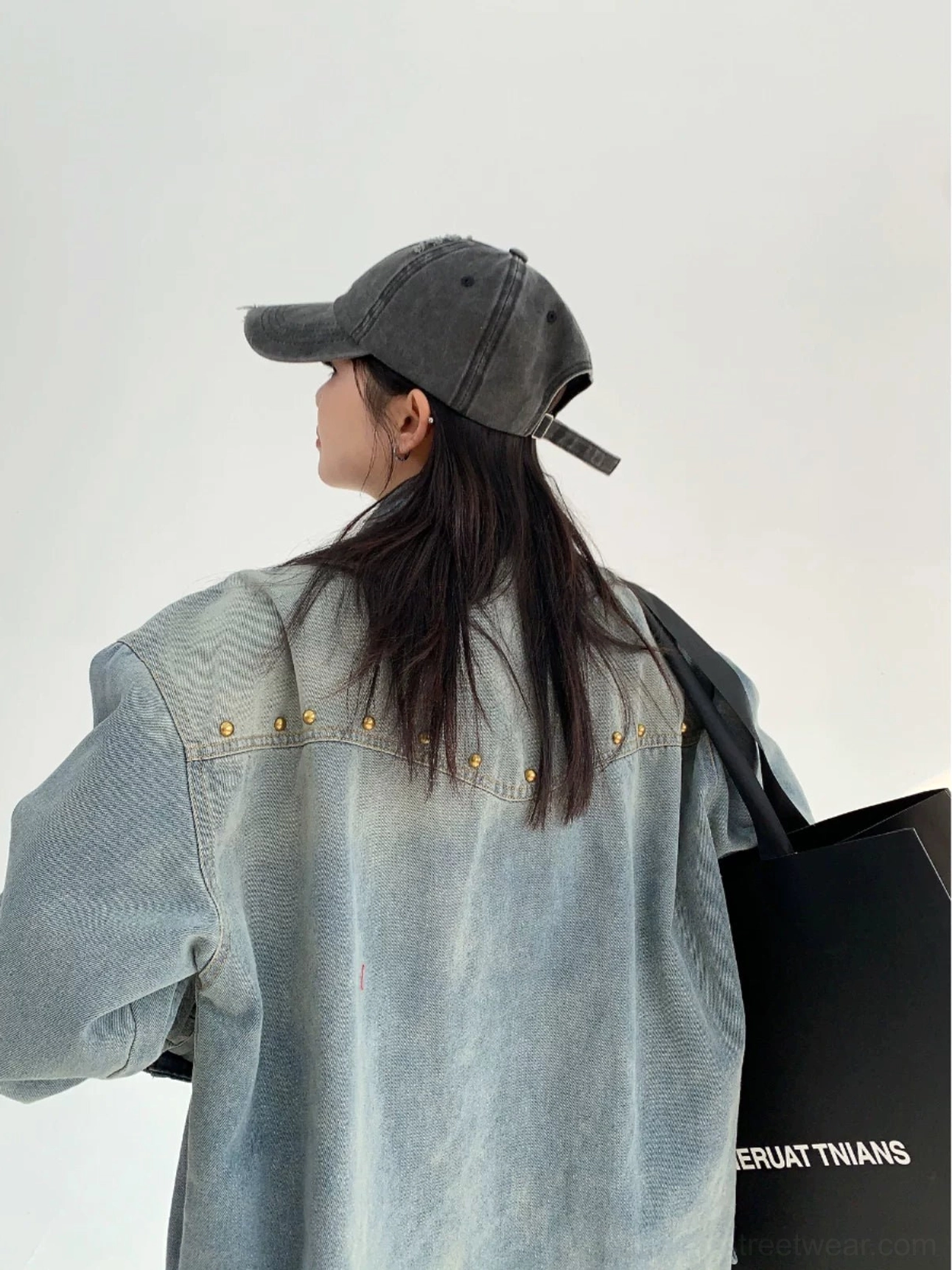 Back view of a faded light blue oversized denim shirt jacket showing gold rivets across the Western back yoke and long loose sleeves