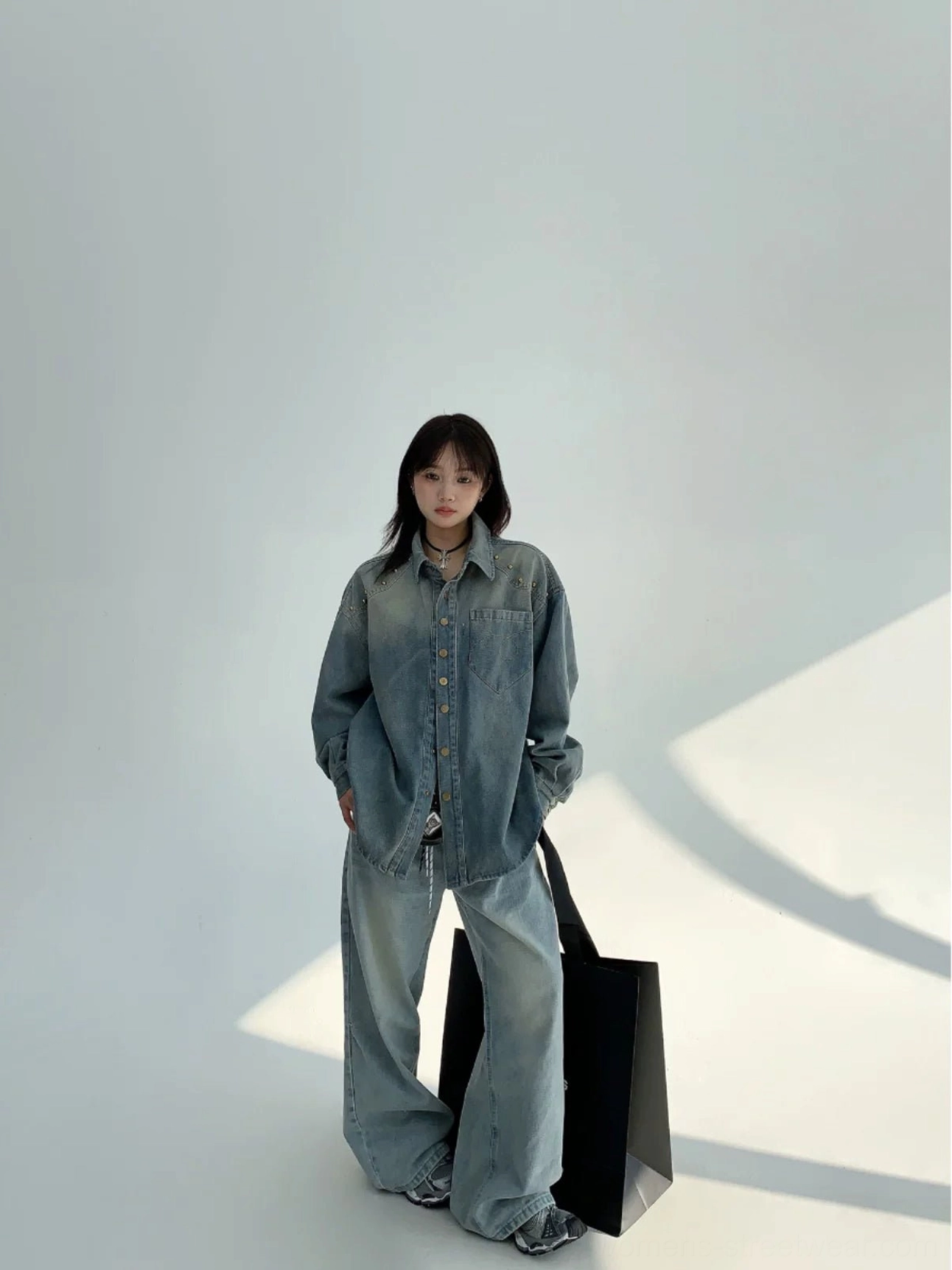 Full-body female model wearing a faded blue oversized denim shirt jacket with matching wide-leg jeans for a coordinated Y2K streetwear outfit