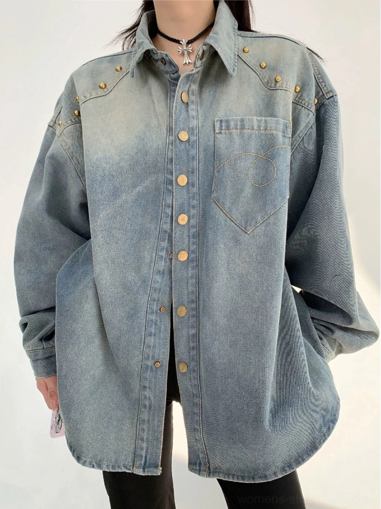 Front close-up of a faded light blue oversized denim shirt jacket with gold shoulder rivets, metallic snap buttons, curved stitched chest pocket, and relaxed streetwear fit