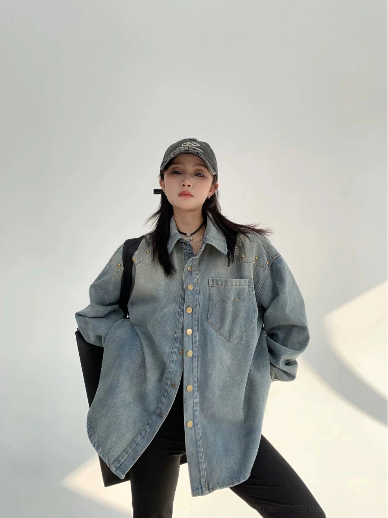 Relaxed three-quarter view of an oversized faded blue denim shirt jacket with chest pocket, rounded hem, and casual baseball cap street style