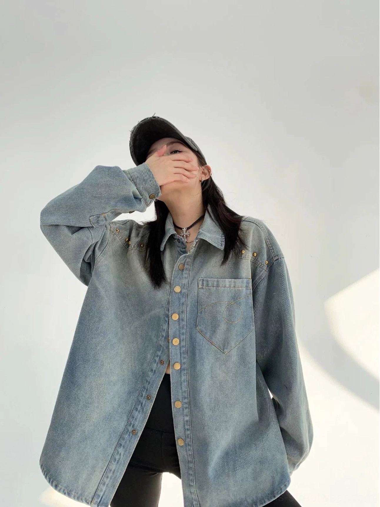 Three-quarter view of a woman in a faded light blue oversized denim shirt jacket with gold rivets, snap buttons, and Korean streetwear styling