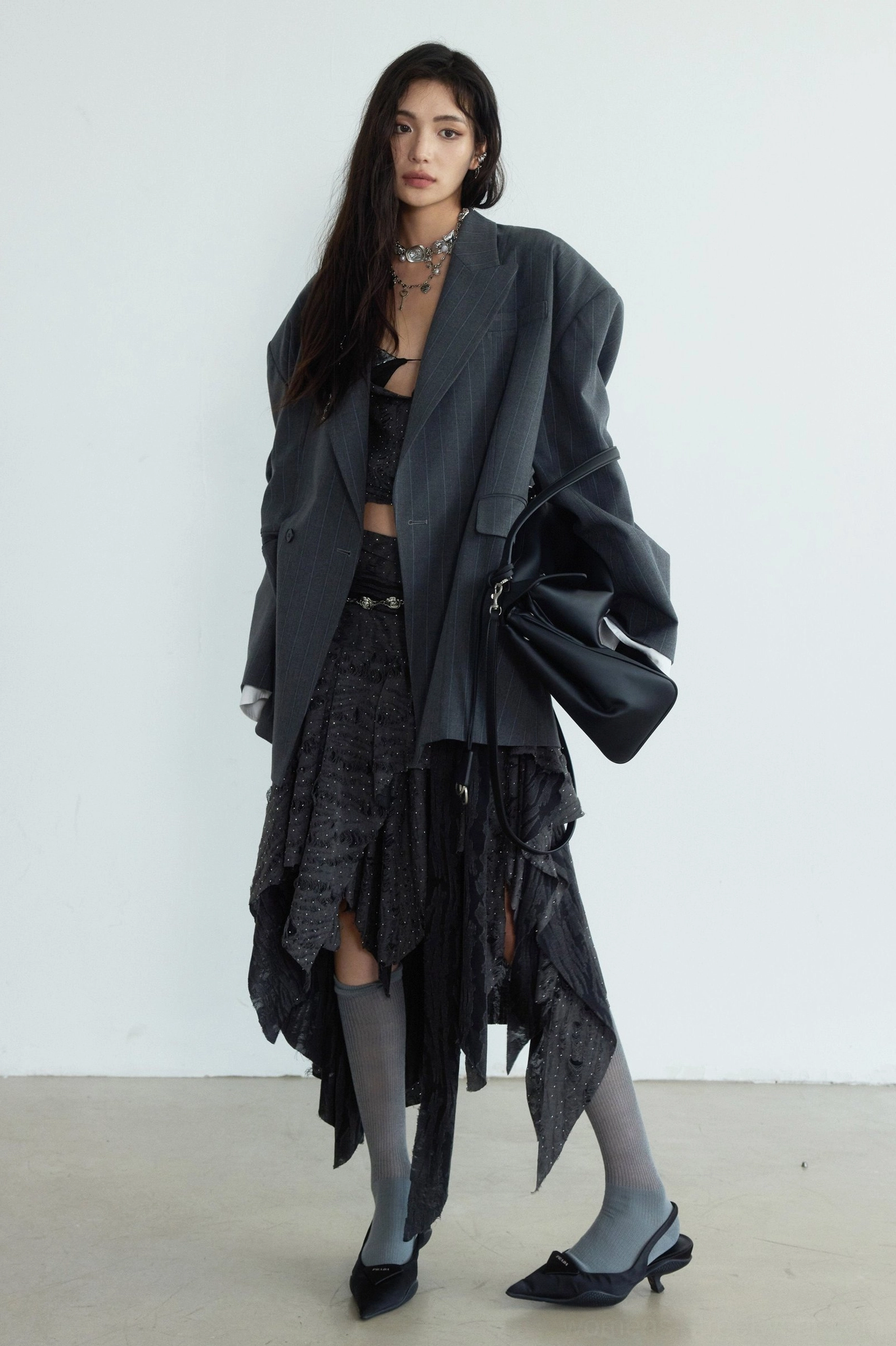 Full front view of a genderless gray striped blazer with oversized fit styled over a dark camisole and ruffled skirt