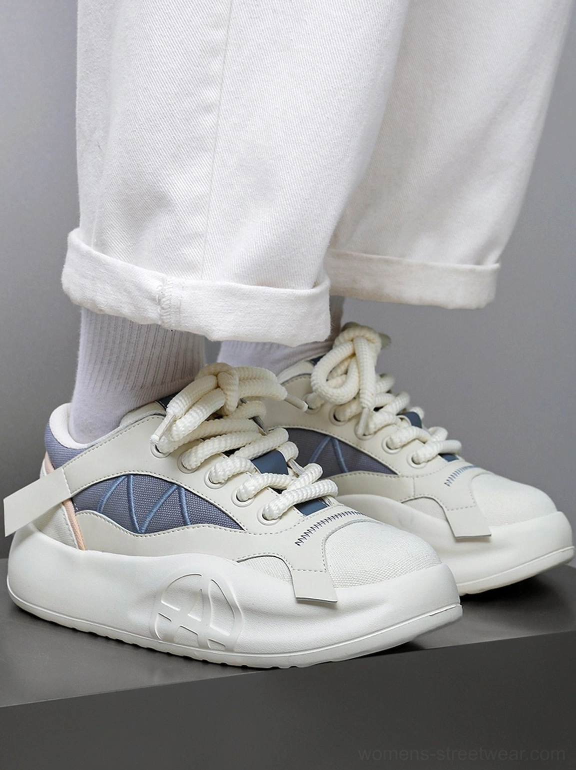 Pair of cream and blue geometric panel platform runner sneakers worn with white trousers, showing the low-top silhouette from the front