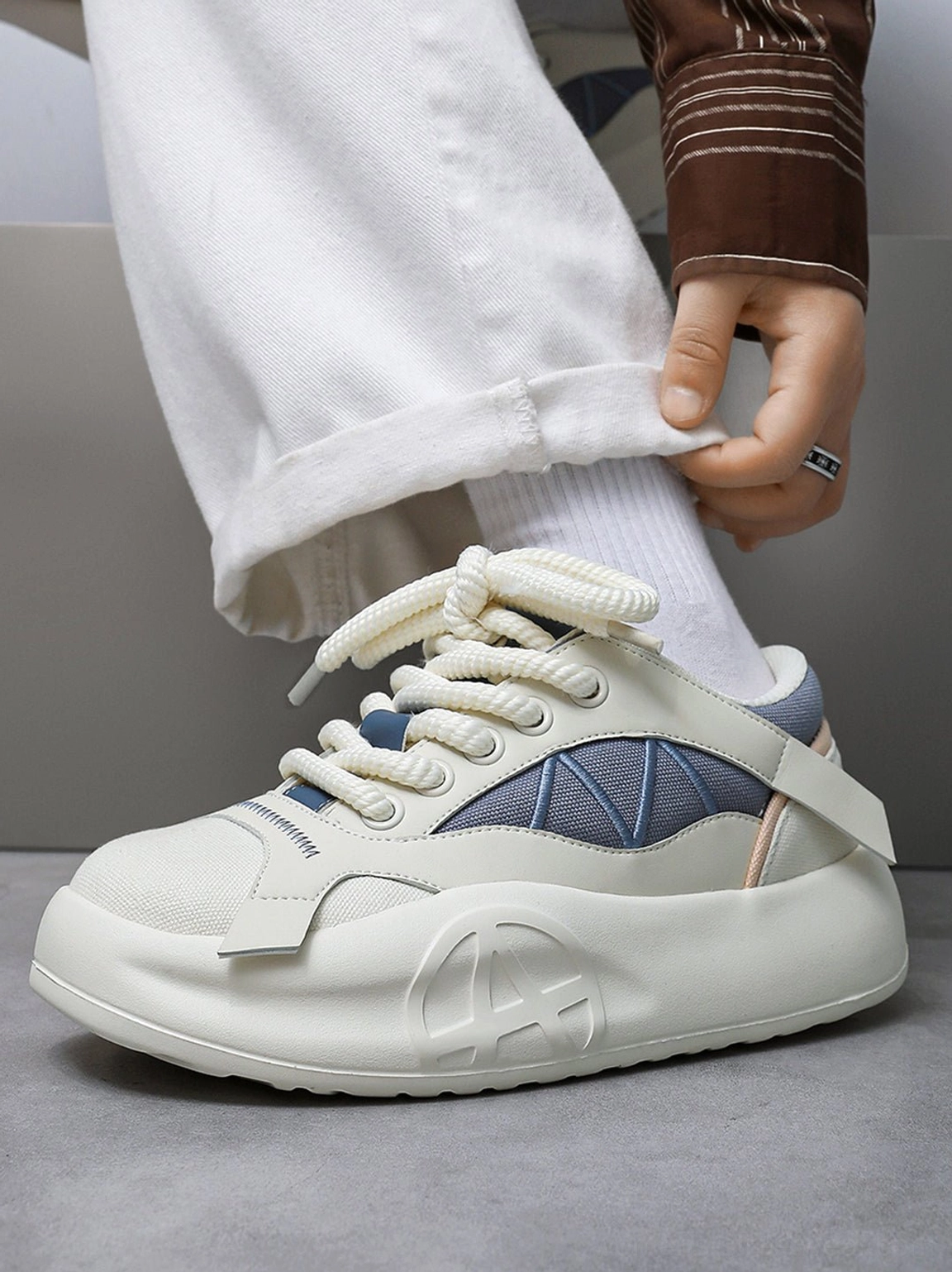 Geometric panel platform runner sneaker worn with rolled white trousers and white socks, showing the laces and upper from a three-quarter angle