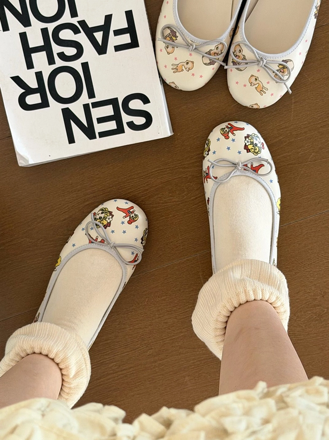 Girl illustrated and puppy printed ribbon square-toe ballet flats displayed with ruffled white crew socks on a wooden tabletop