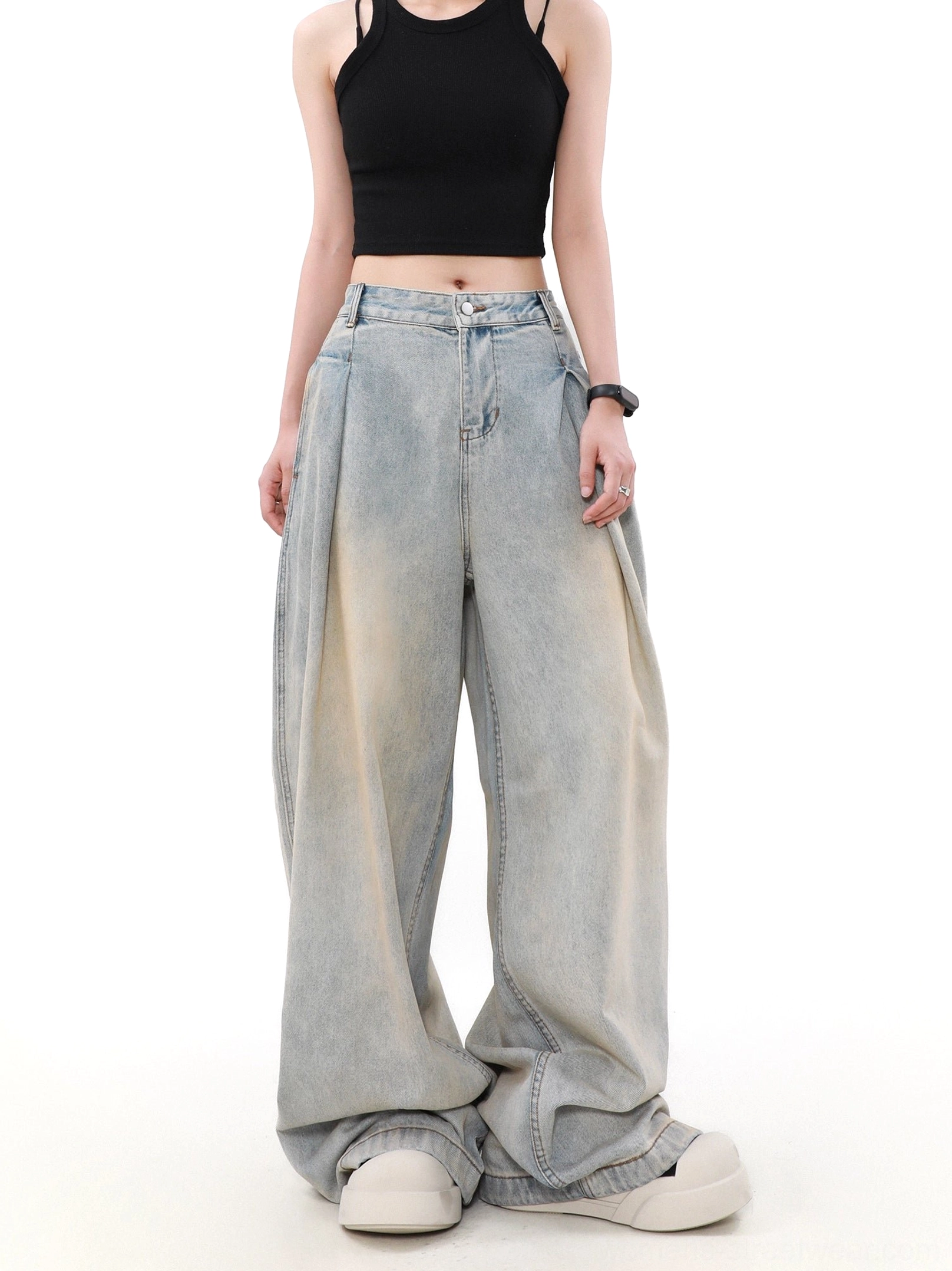 Left front three-quarter view of high-waisted pleated denim jeans with dramatic wide legs, vintage wash, and platform sneaker styling