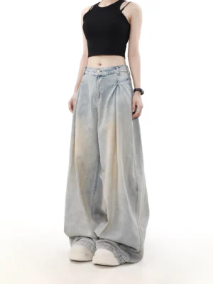 Front three-quarter view of women’s faded light blue ultra-wide pleated jeans styled with a black cropped camisole and white platform sneakers