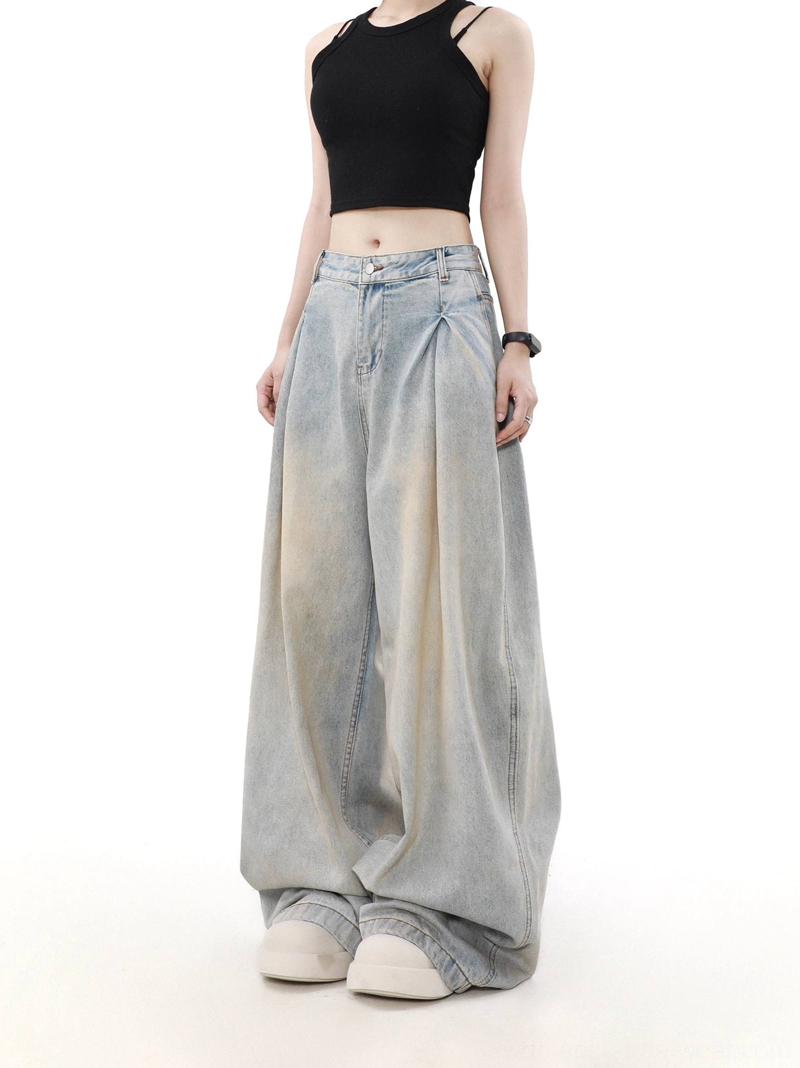 Front three-quarter view of women’s faded light blue ultra-wide pleated jeans styled with a black cropped camisole and white platform sneakers
