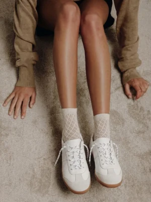 Light beige low-profile retro trainers worn with knit socks and casual cropped streetwear styling in an overhead lifestyle view