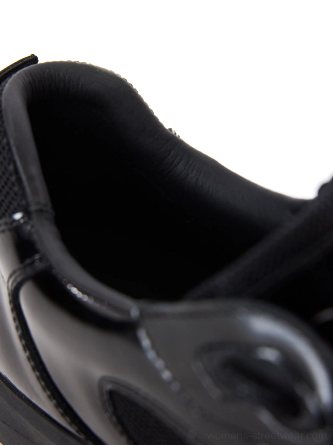 Close-up of glossy black leather sneaker interior, smooth lining, heel construction, and precise stitching details
