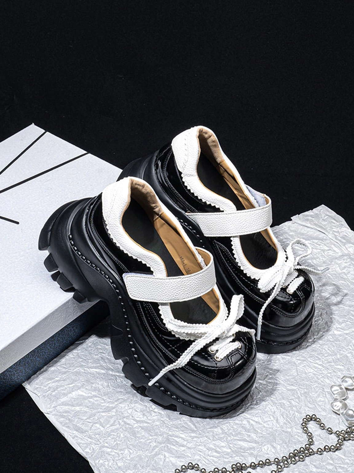 Rear three-quarter view of glossy black platform Mary Jane shoes with white straps and a bold chunky platform outsole