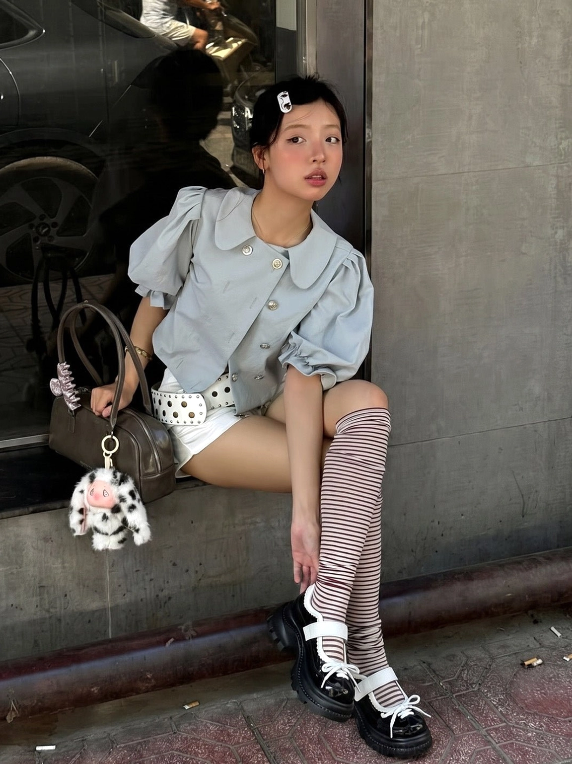 Side view of women's chunky platform Mary Jane shoes with contrast straps styled with white shorts and striped socks outside a storefront