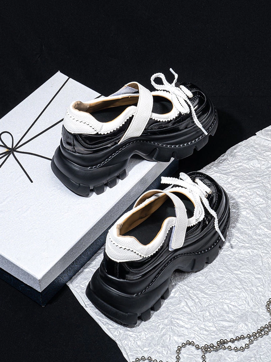 Side overhead view of glossy black and white platform Mary Jane shoes showing the structured silhouette, adjustable straps, and thick platform sole