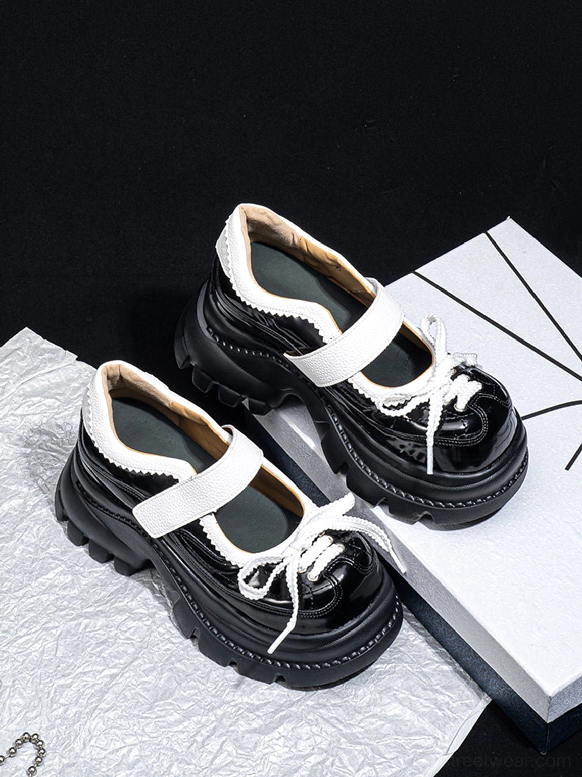 Oblique overhead view of glossy black platform Mary Jane shoes showing the white contrast straps, bow lace detail, rounded toe, and polished upper