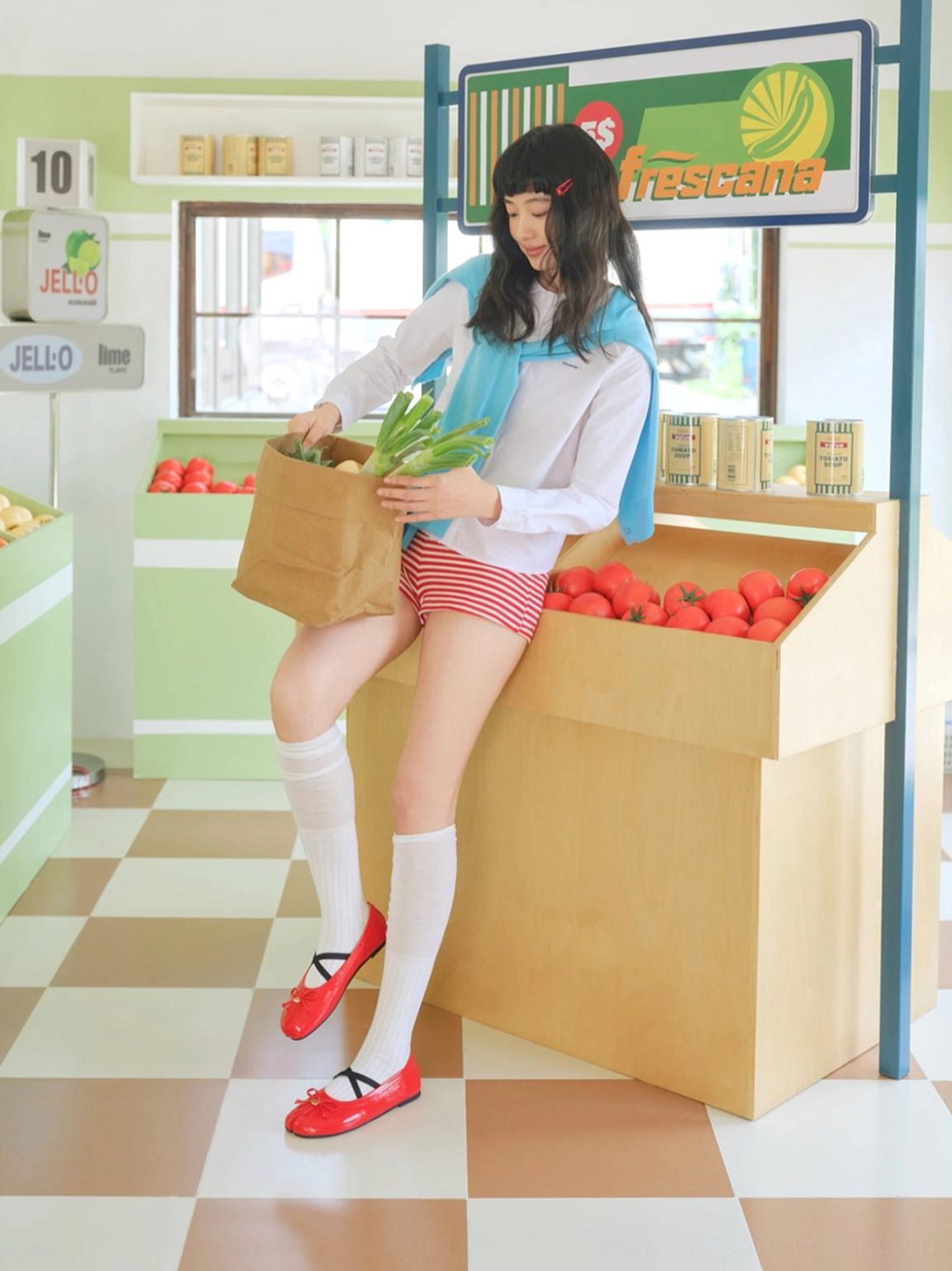 Seated model wearing glossy red split-toe Mary Jane ballet flats with bow detail and white over-the-knee socks