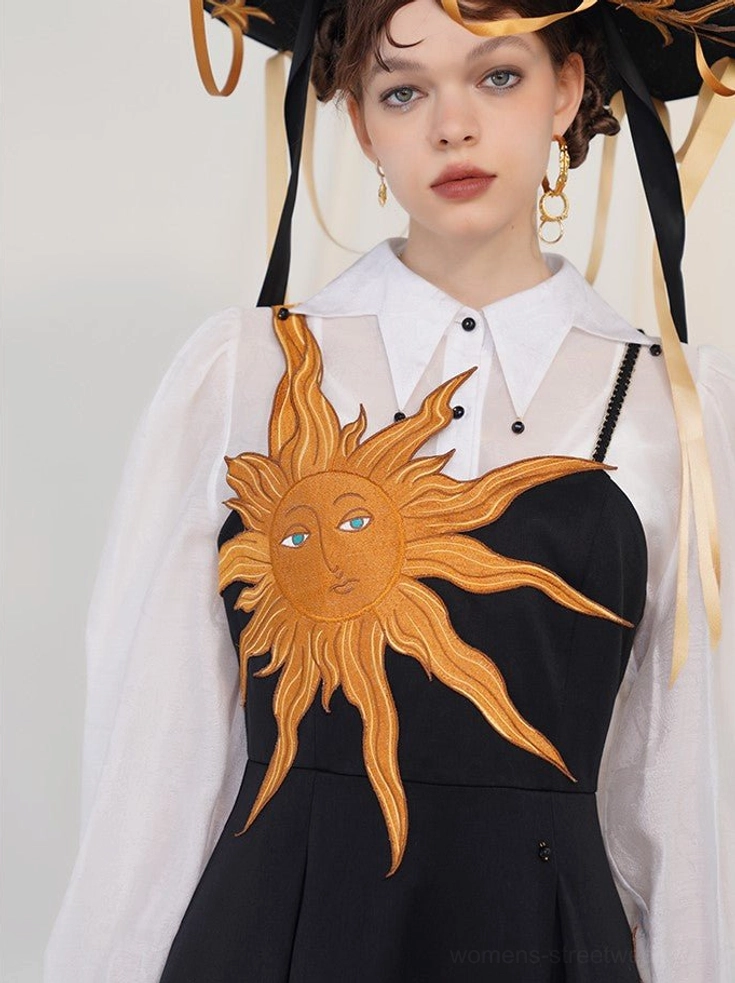 Detailed upper body view of golden sun embroidery on a black slip dress with camisole straps and sheer white collared shirt