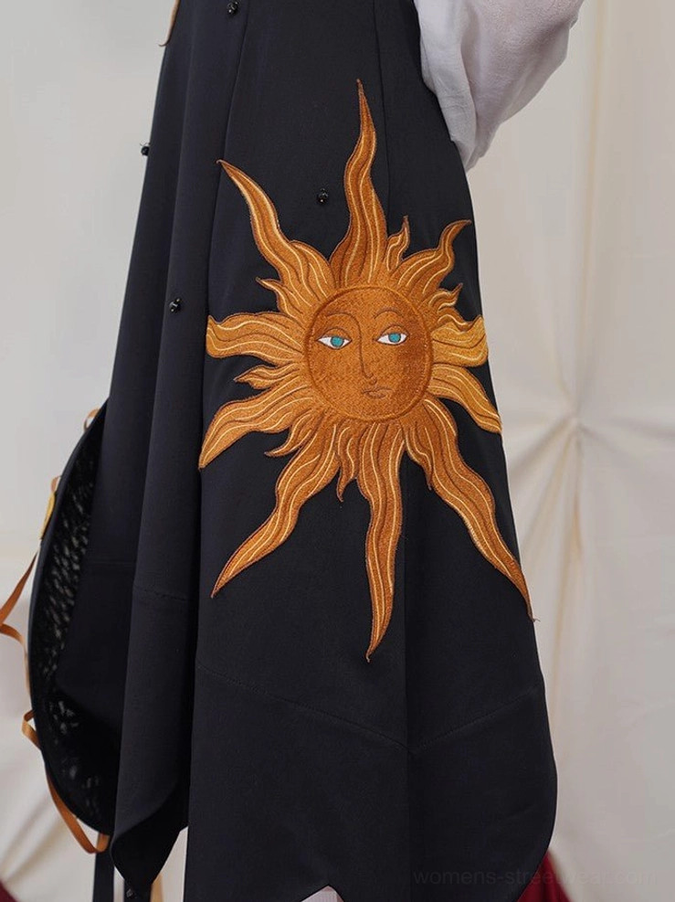 Close-up detail of large golden sun face embroidery with blue eyes and decorative bead accents on black dress fabric