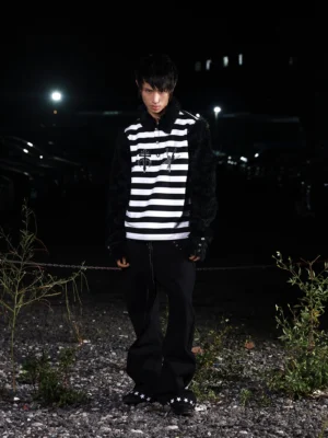 Front view of a black and white striped gothic streetwear long sleeve shirt with black faux fur collar and sleeves, chest sigil embroidery, and dramatic punk styling