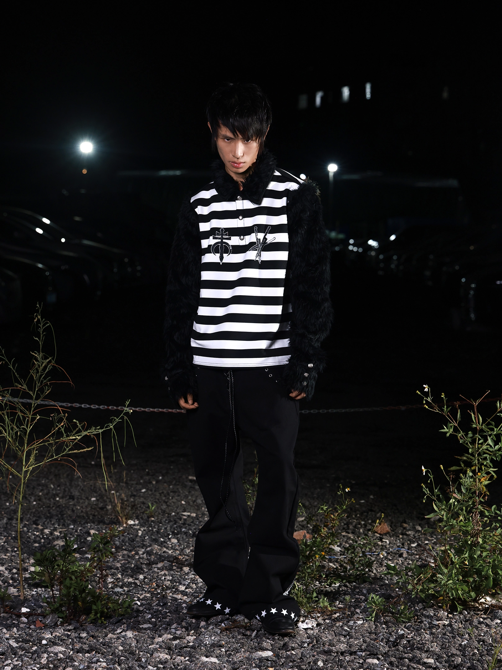 Front view of a black and white striped gothic streetwear long sleeve shirt with black faux fur collar and sleeves, chest sigil embroidery, and dramatic punk styling