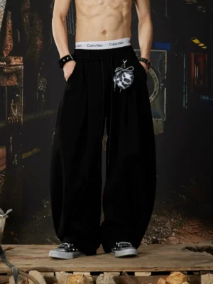 Black gothic wide-leg sweatpants with elastic waistband side pockets and decorative leopard-print fuzzy charm in a streetwear studio setting