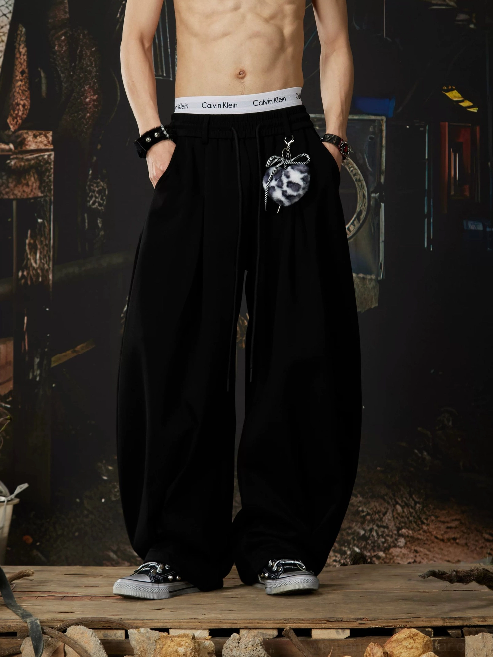 Black gothic wide-leg sweatpants with elastic waistband side pockets and decorative leopard-print fuzzy charm in a streetwear studio setting